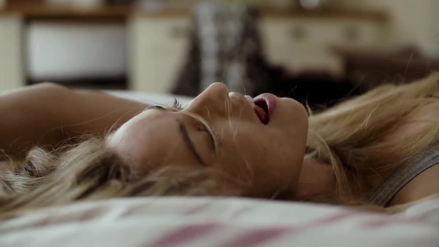 A blonde woman dances and sings in bed
