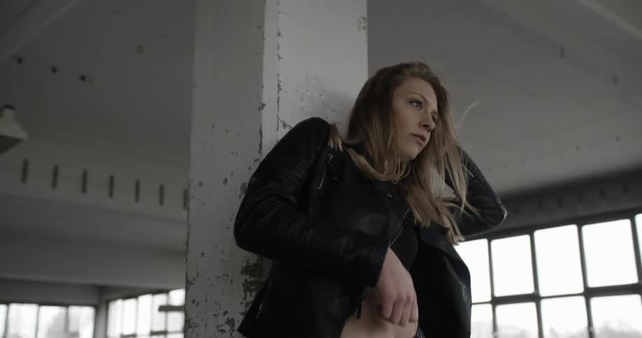 A woman in a jacket dances in front of a chipped pillar