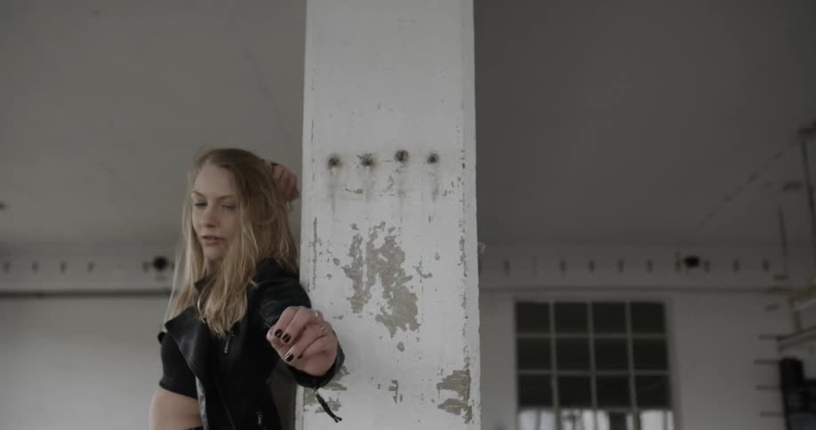 A woman brushes her hair and reaches out near a pillar