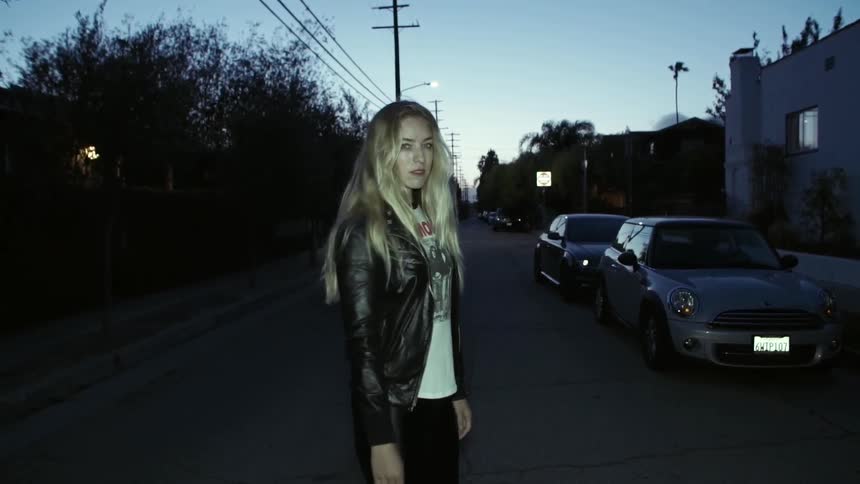 A woman standing in a street turns and walks away from the camera