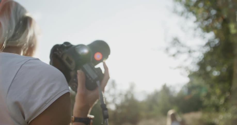 Blonde woman holding her camera while looking at her subject in the distance