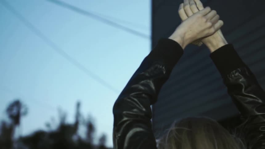 A blond woman walks down a darkened alley and raises her hands over her head