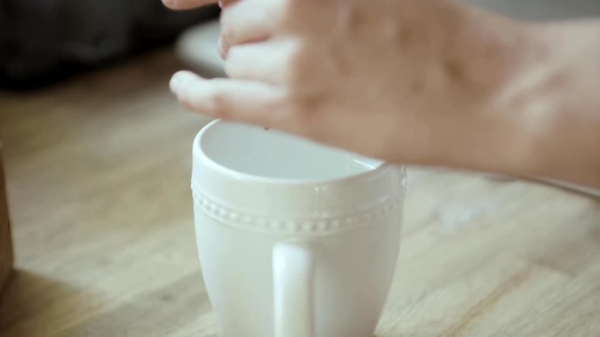 A person drops coffee grounds into a mug of water