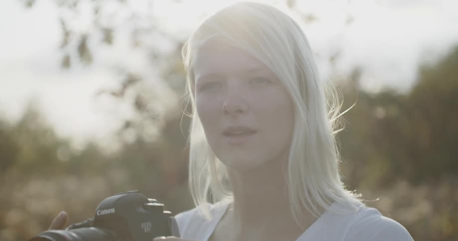 A woman standing outside on a cloudy day lifts a camera