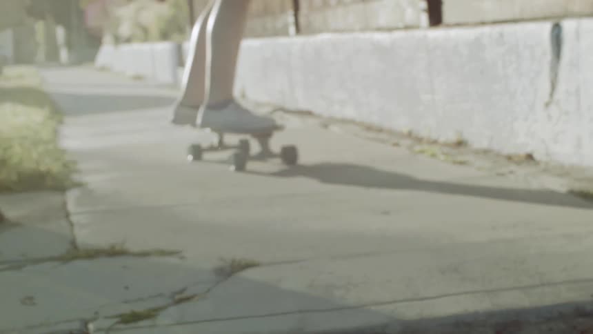 Person skateboards down a sidewalk and off a small curb