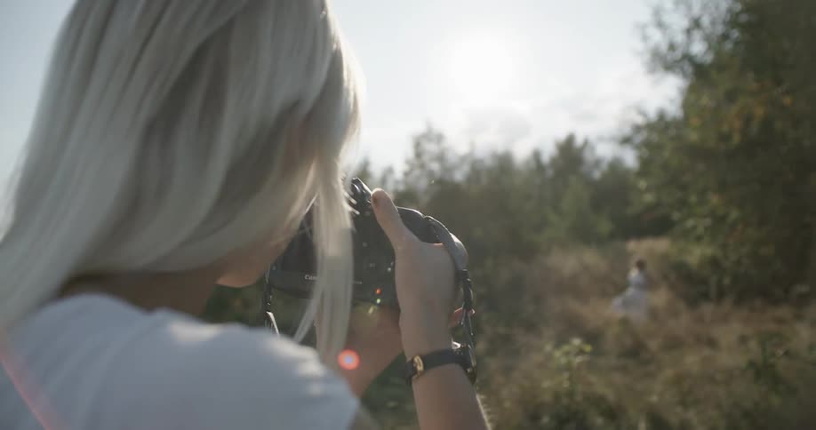 A woman is photographing someone on a grassy hill
