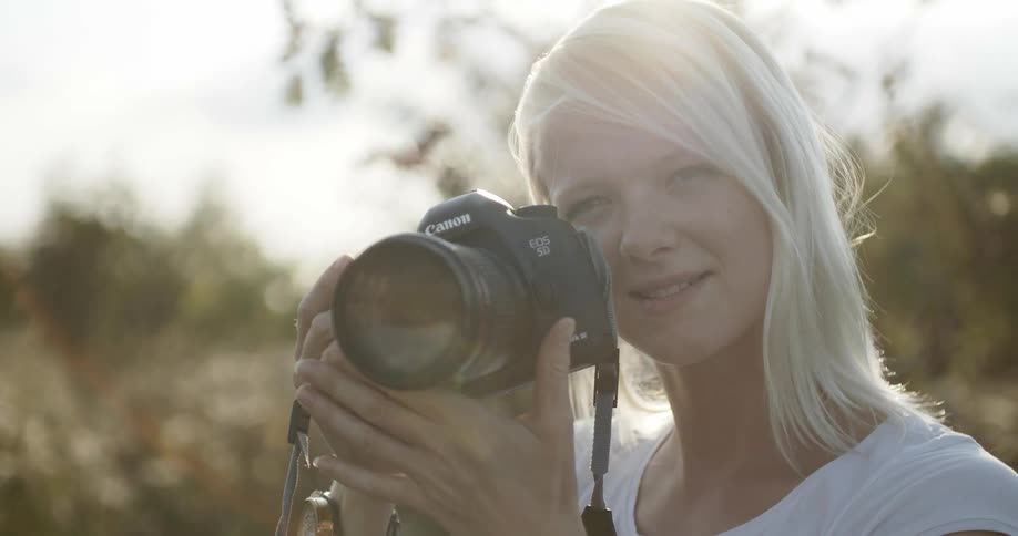 A woman with blond hair gestures and points a camera
