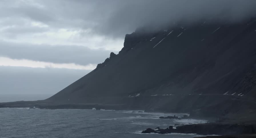 Small waves coming ashore on a dark beach on a very cloudy day