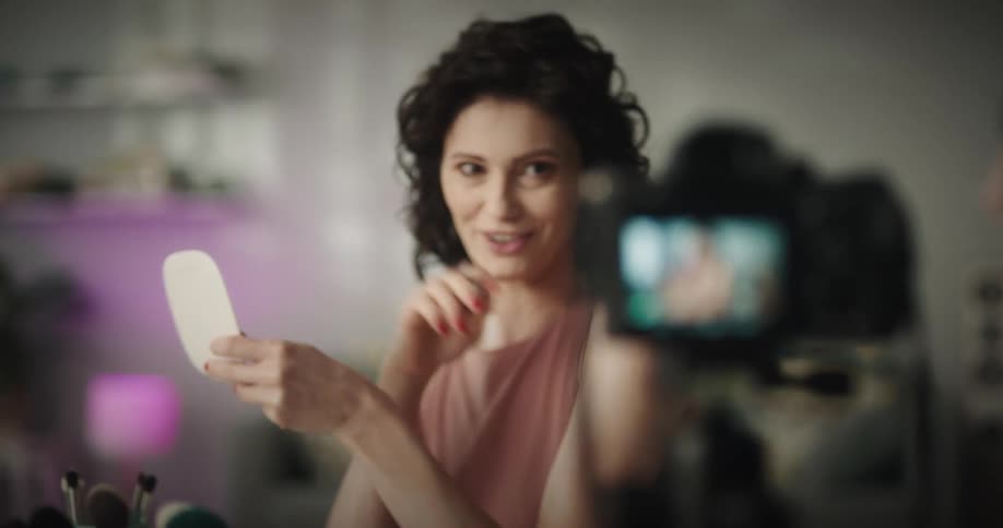 A woman sitting in front of a camera is recording a video of herself talking about makeup