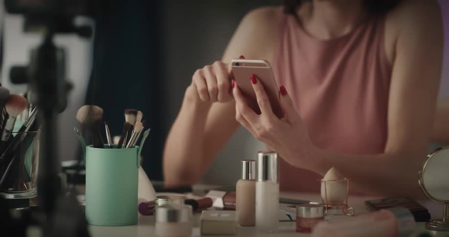 Closeup of woman sitting at make up table scrolling on cell phone