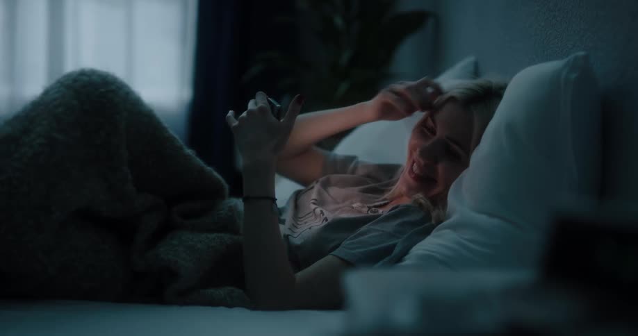 Blonde female laughing and texting on cell phone while laying in bed