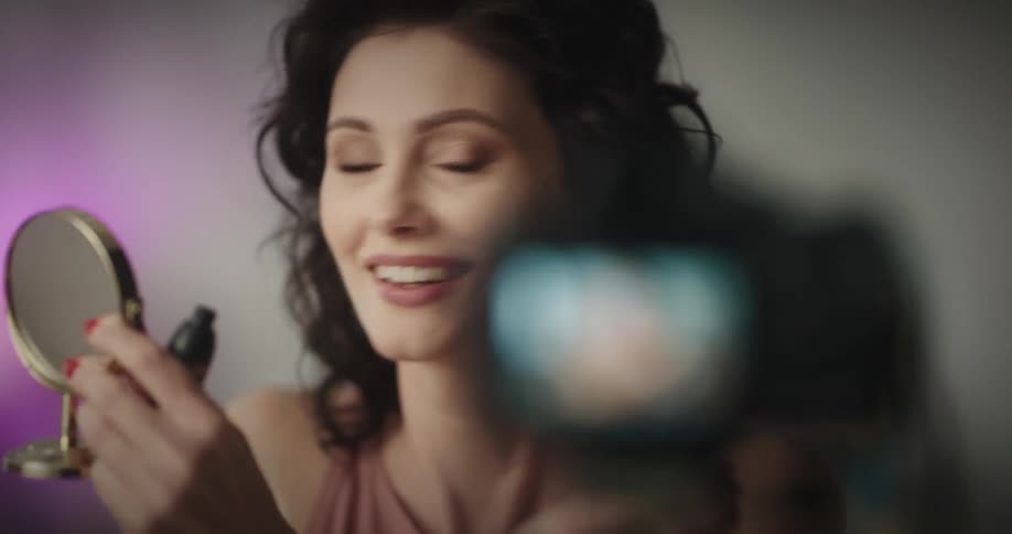 A woman is applying makeup in front of a video camera