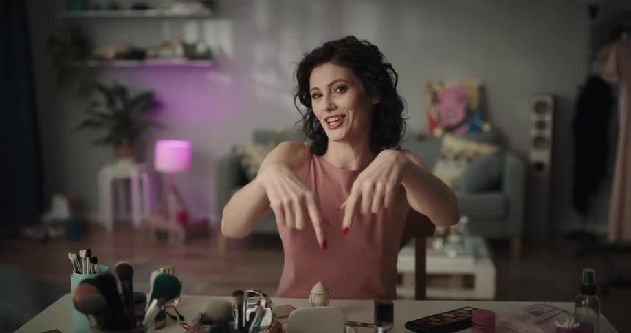 Woman sits applying makeup and talking to the camera