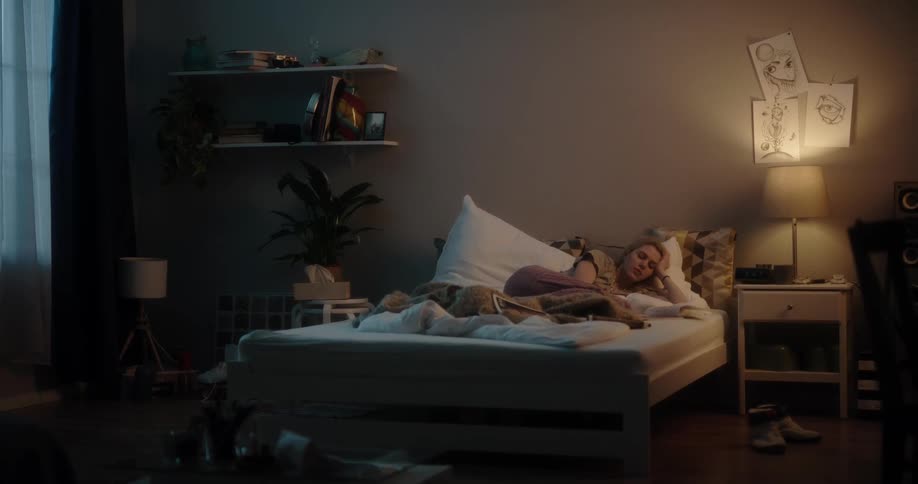 Young white woman lying in her bed and reading a magazine in her bed