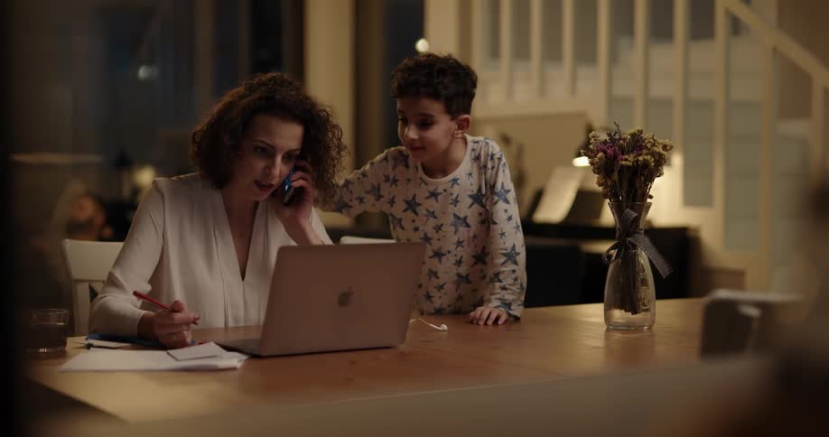 A little boy comes down stairs with his puppy trying to get his frazzled mothers attention while she works