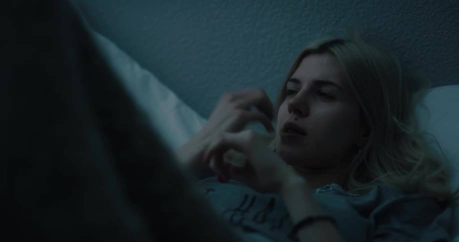 Young white woman lying in bed bitting her nails and then taking her smartphone and smiling