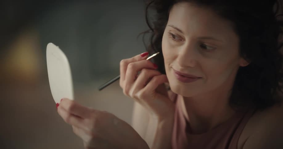 Happy woman holding a mirror on her hand applies make up on her face