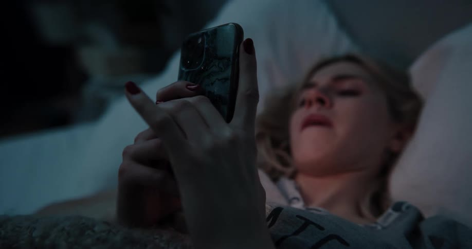 A woman is laying in bed while texting on a smartphone at night