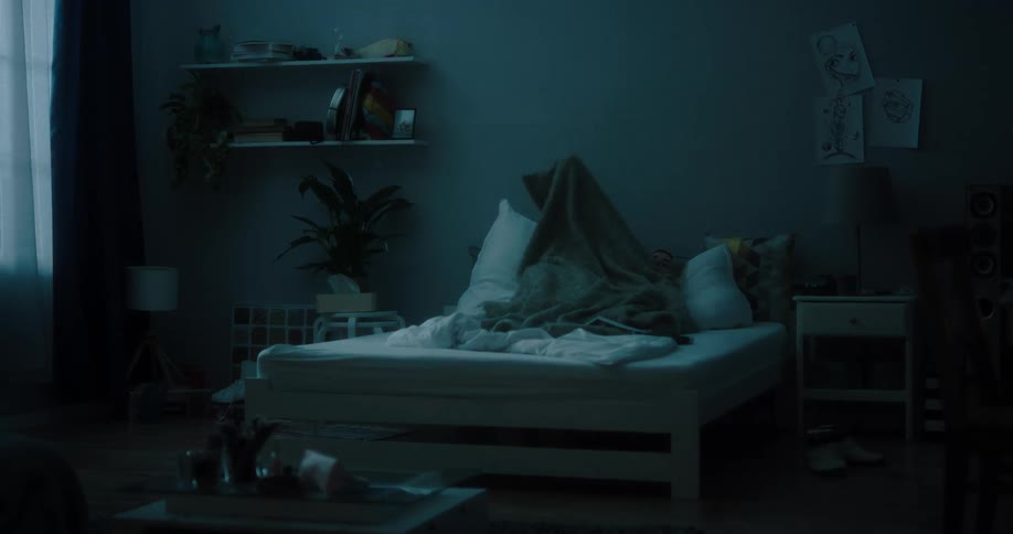 Blonde woman gets under blanket on bed at night in bedroom