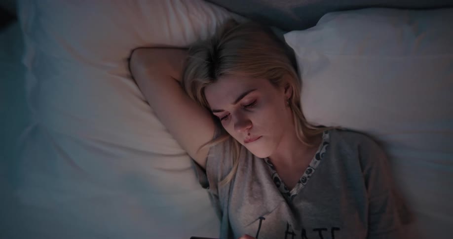 A woman bites her lip as she looks at her phone while in bed