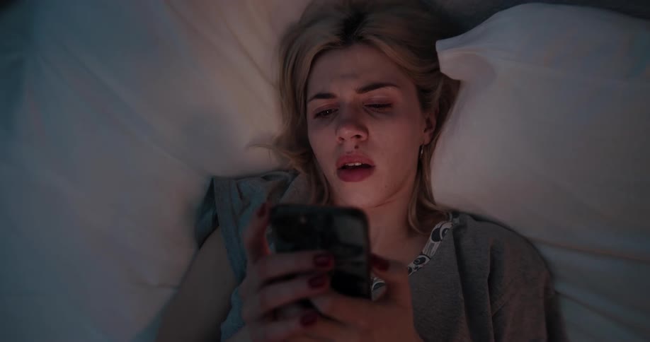 A woman laying in bed on a smartphone