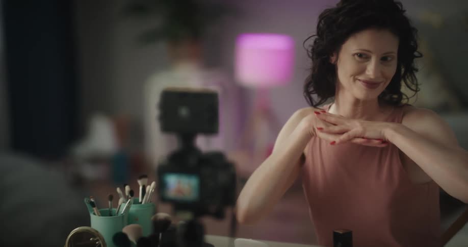 A woman is filming herself talking with makeup all around