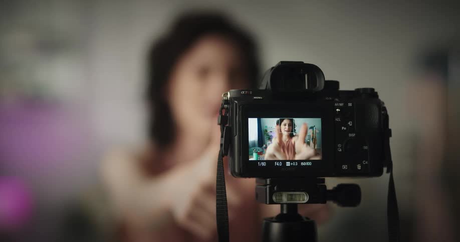 A woman is sitting indoors in front of a video camera while making a social media video