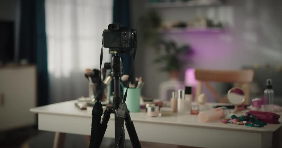 A camera on a tripod is set up aimed at a table with makeup and cosmetic items