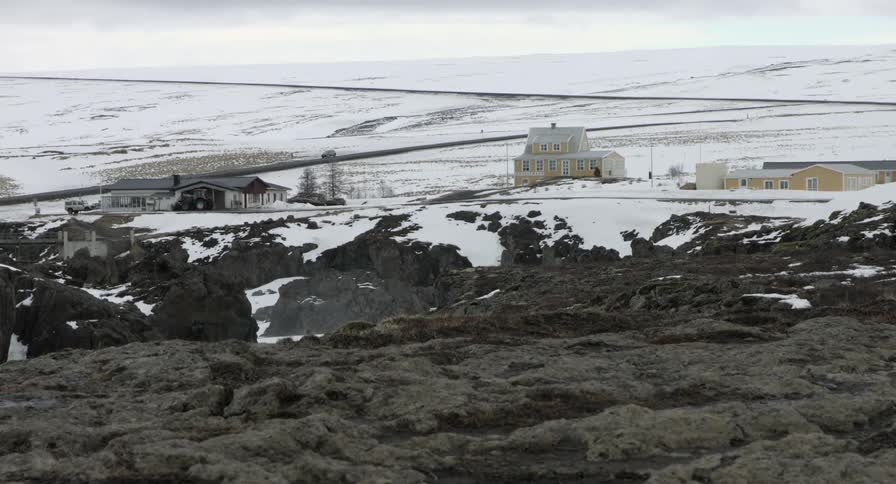 A car is traveling in the distance near a hilly area covered with snow