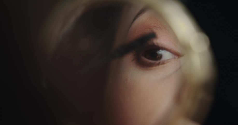 Woman looking in hand mirror puts on makeup