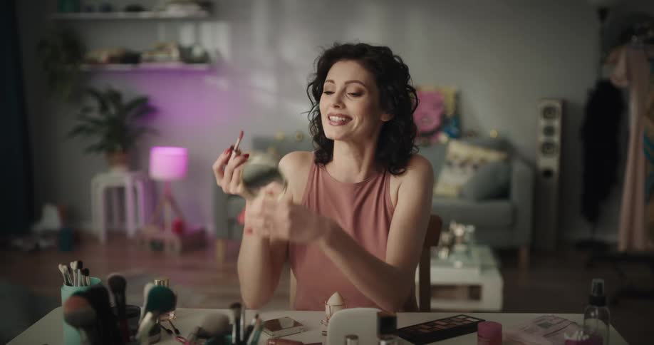 A woman talks as she shows make up and then applies it