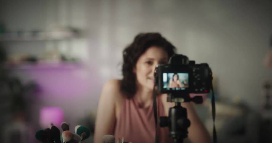 Woman applies makeup while talking and recording herself with a camera on a tripod