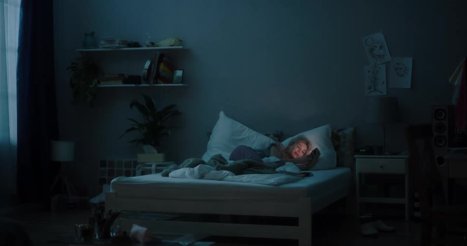 Young woman talking on her smartphone while laying in bed at night
