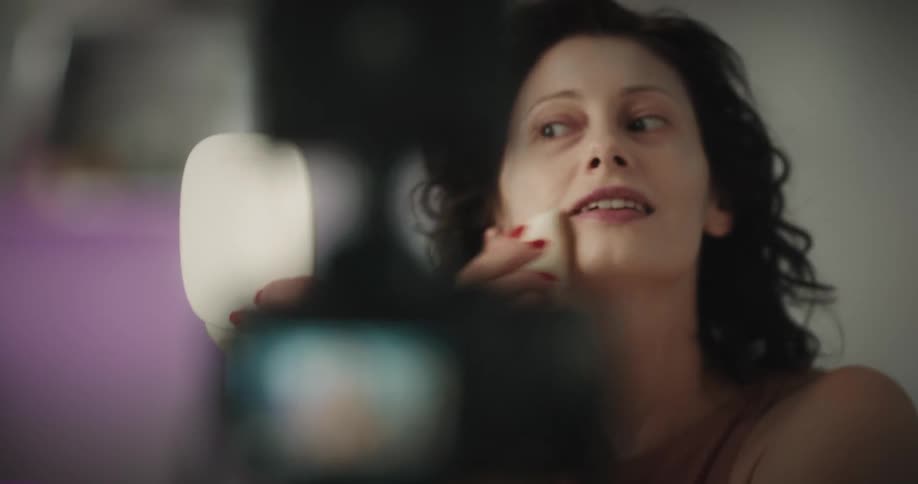 A woman is putting on makeup in front of a camera