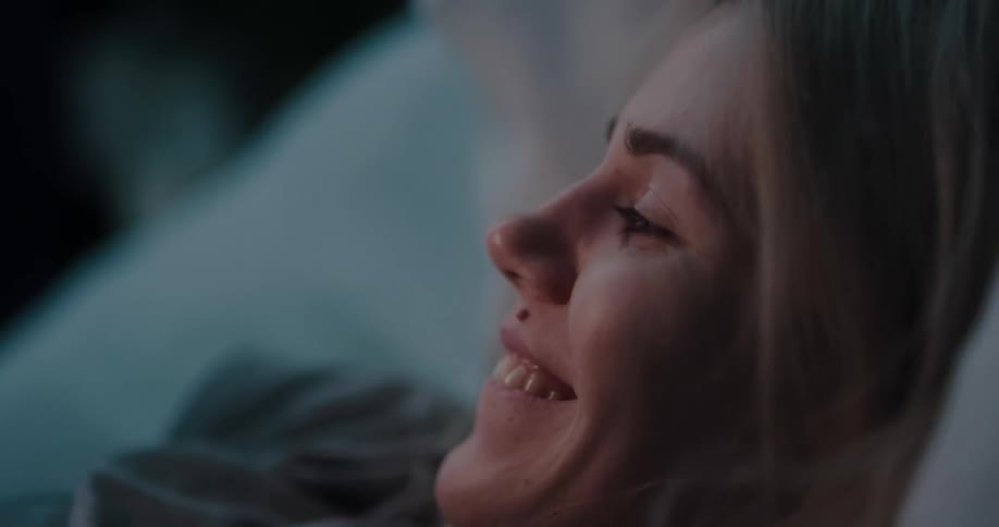 A woman smiles to herself while texting in bed