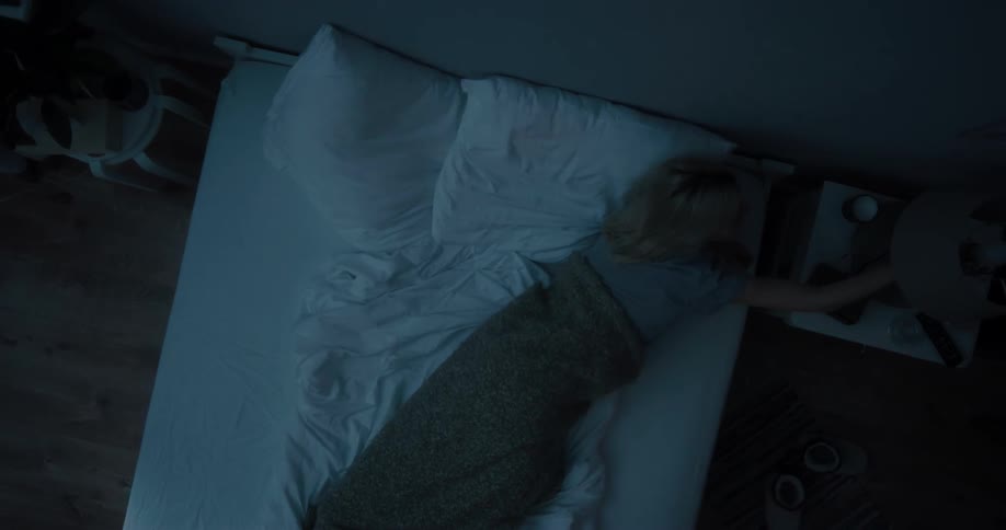 White woman lying down in bed sleeping and then waking up and turning on the table lamp
