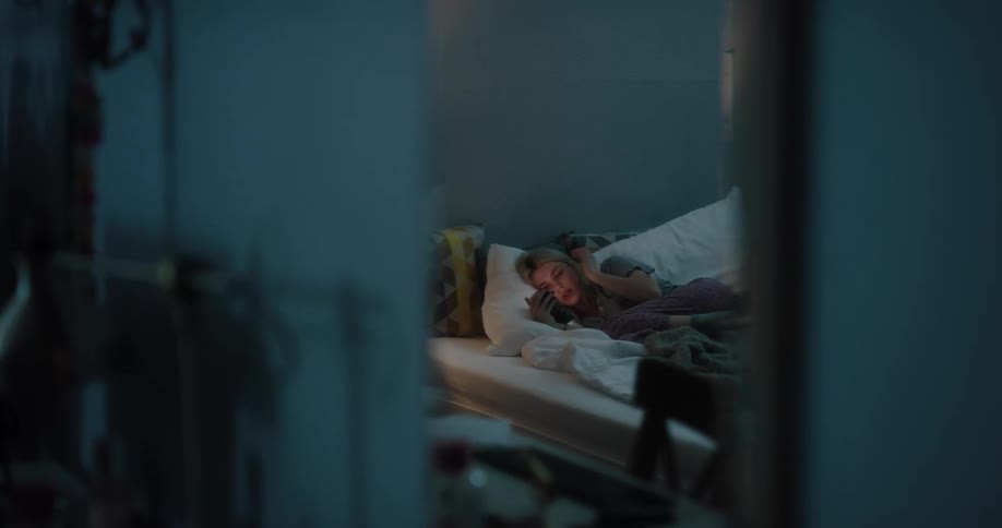 Teenaged girl lays in her bed and looks at her cell phone