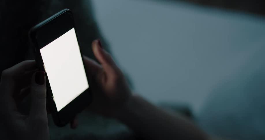Woman lying in bed uses smartphone in bedroom