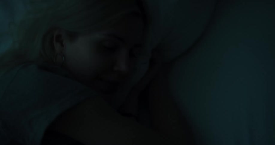 A young woman lying in bed smiles while using her smartphone before tucking the phone beneath her pillow and going to sleep