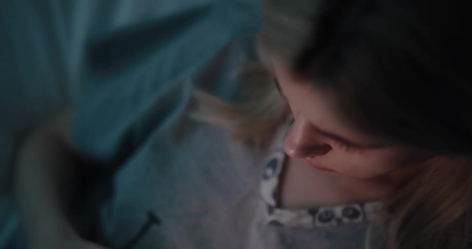 Young white woman lying in her bed and typing on her smartphone during night