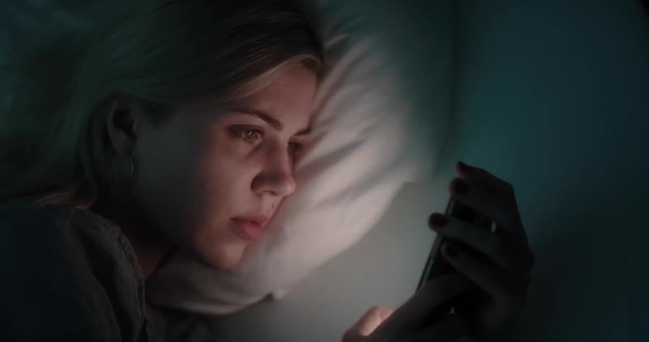 A woman is laying down and texting in bed