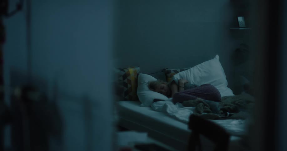 A teenage girl with her arms wrapped around herself lies in bed