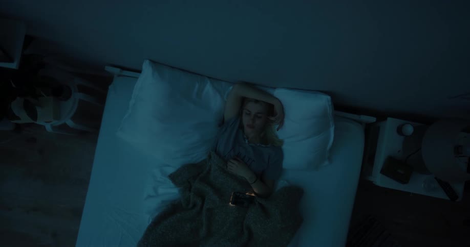 A woman pulls her cell phone out in bed