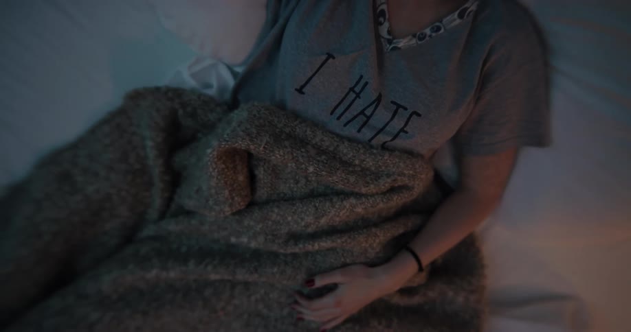 A woman lying in bed under a blanket with her phone beside her