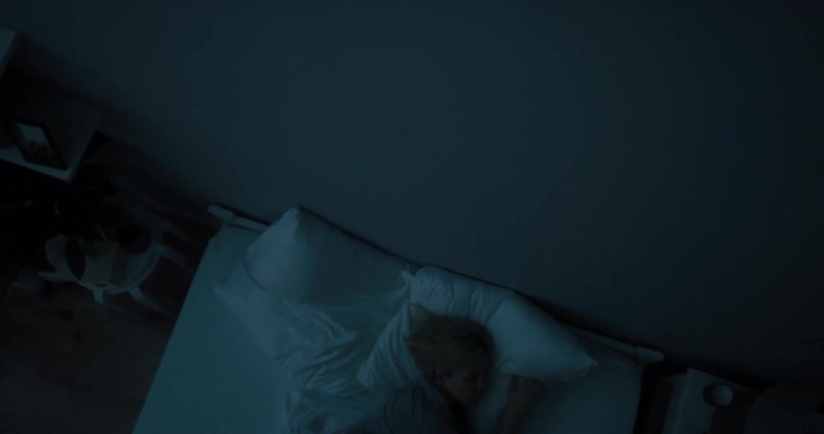 A woman tosses and turns while trying to sleep in a dark bedroom