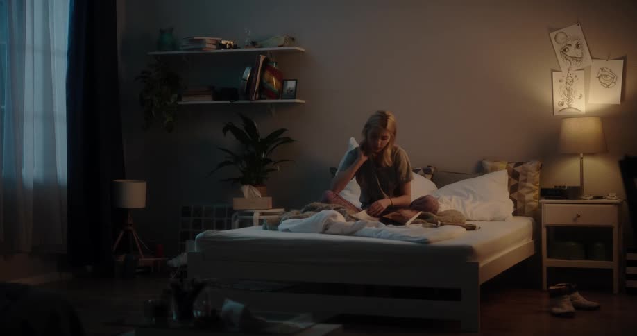 Young blonde woman sitting over a bed in the bedroom at home reading a magazine at night