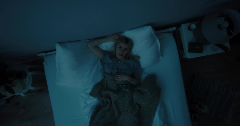 A woman lying in bed on her back unable to sleep with her phone on top of the blanket