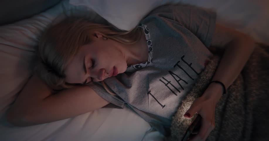 A woman scrolls through her phone while lying in bed