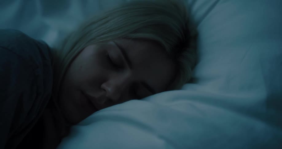 A woman sleeps with her head on a pillow in a dark room
