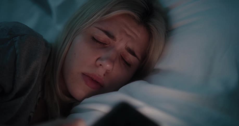 Young white woman lying in bed and waking up then grabbing her smartphone and typing